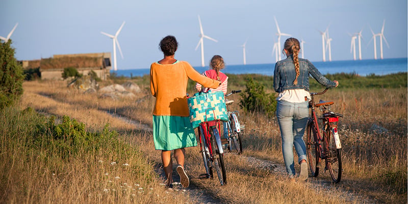 En mamma och två barn med cyklar och vindkraftverk i bakgrunden.