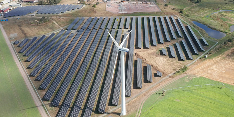 Solpark med ett vindkraftverk framför.